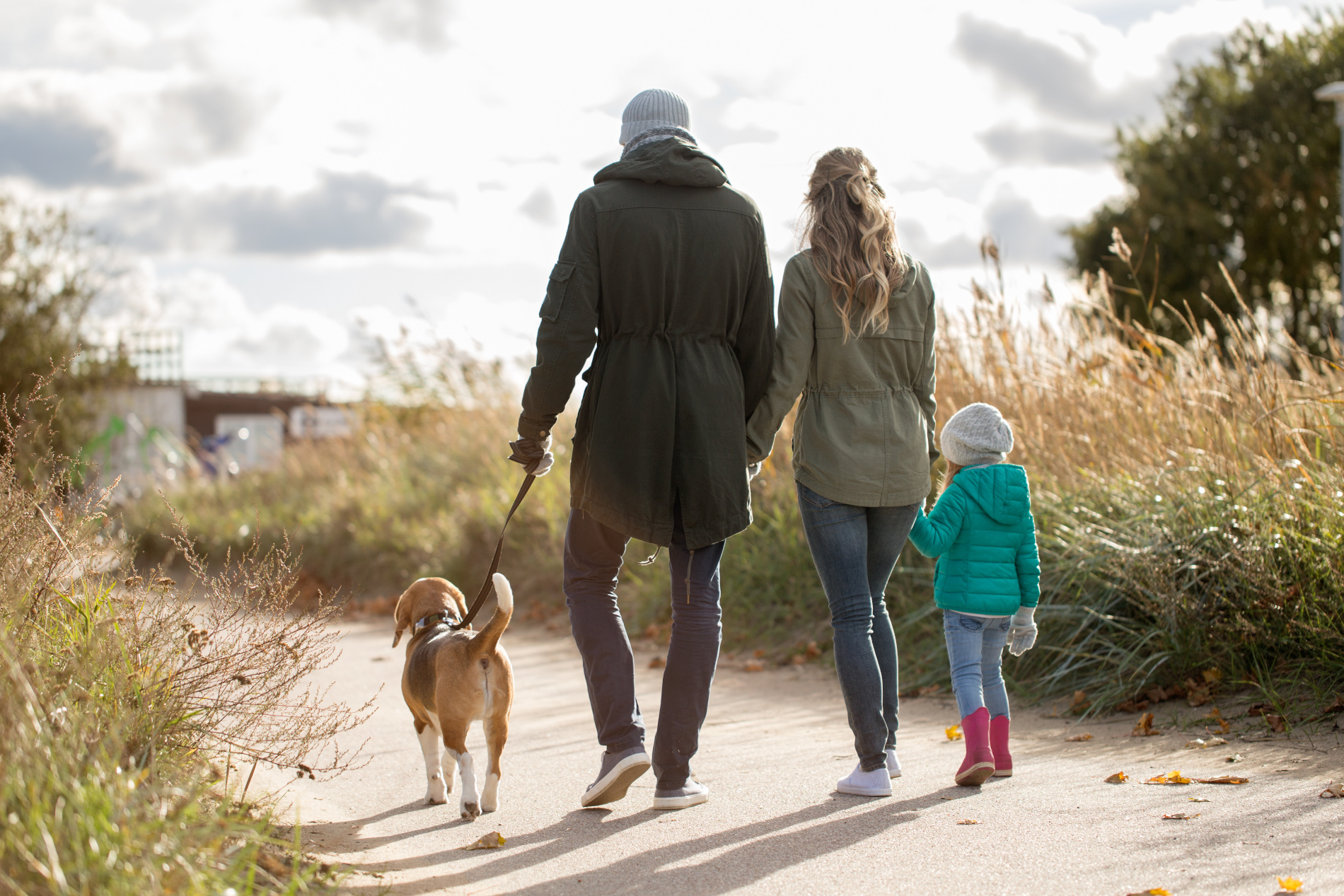 Família de 3 pessoas, dois adultos e uma criança, passeio com o seu cão num caminho na natureza.
